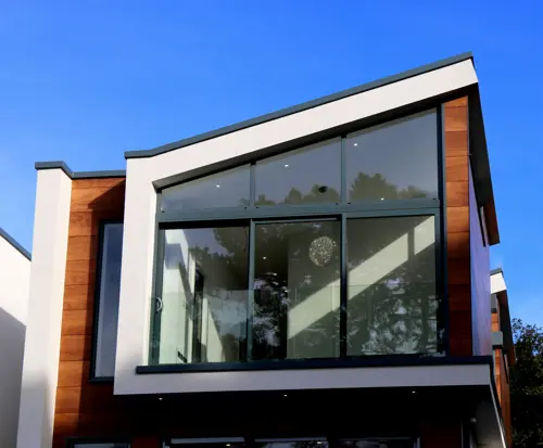 logo Modern tvåplans villa med stora glaspartier, träpanel och vit putsfasad mot blå himmel.