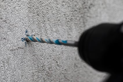 Borr skär in i betongvägg, med blå borrspån runt hålet.