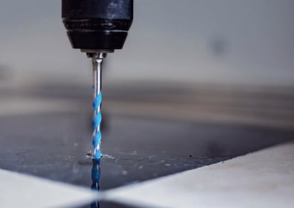 Borrmaskin med blå-vit borr genomtränger en reflekterande yta.