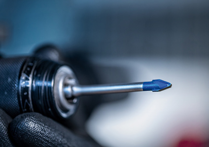 Elektrisk borr med en borrliknande spets täckt av blå plast, hålls av hand i svart handske.