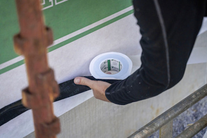 En person som applicerar tätningsband på en byggvägg. En ställning och rulle med vitt band syns.