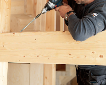 En person borrar i en träbalk med en elektrisk borrmaskin.