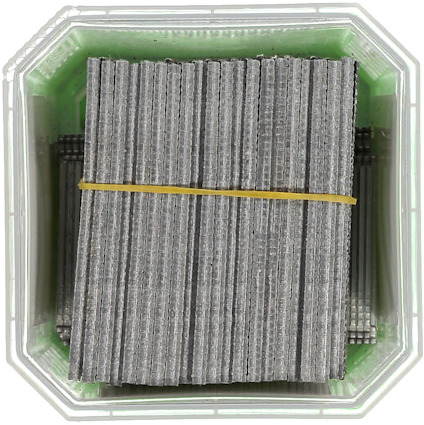 Staples neatly stacked in a green container secured with a yellow rubber band.