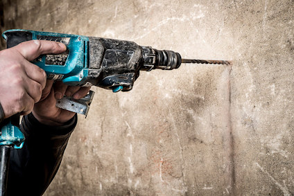 Händer håller en borrmaskin mot en betongvägg.