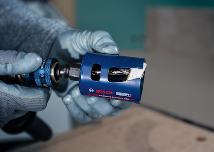 Två händer i handskar håller ett blått sågblad med texten "BOSCH" och "EXPERT".