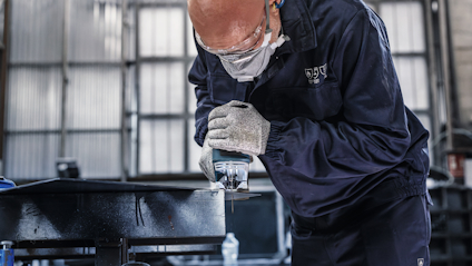 Person i skyddsutrustning svetsar metall i industrimiljö.