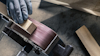 Hand med skyddshandske slipar träbit mot roterande slipband.