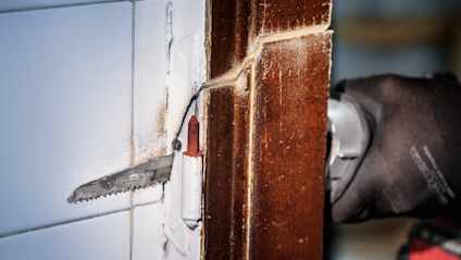 Hand som håller ett oscillerande verktyg med sågblad mot en trä- och kakelyta.