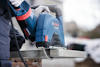 En person använder en blå Bosch kapmaskin för att skära i en betongplatta.