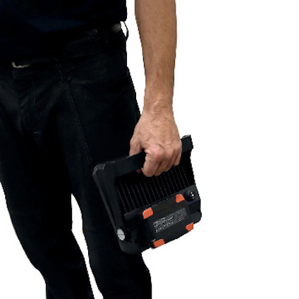 En person håller en svart och orange handhållen apparat med knappar och rattar.